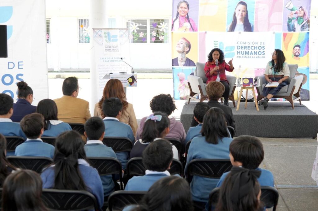 Niñas y niños de primaria escuchan con atención la presentación del cuento “Meztli”, rodeados de carteles y materiales educativos sobre menstruación digna y salud emocional.
